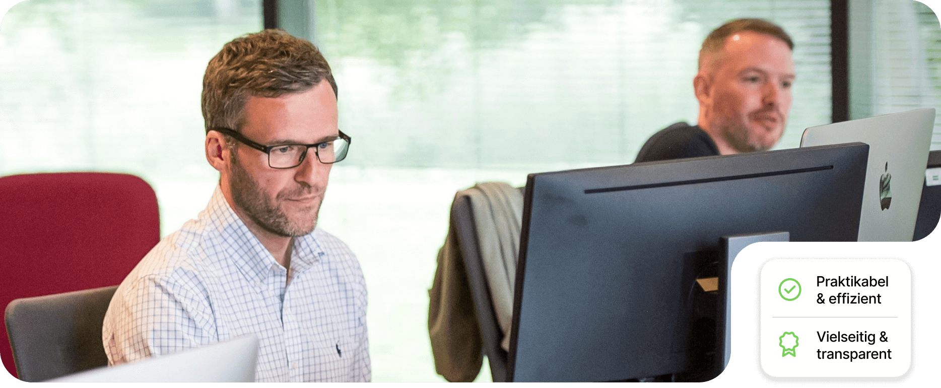 Two men working diligently at their computers in a modern office setting, focused on their tasks.