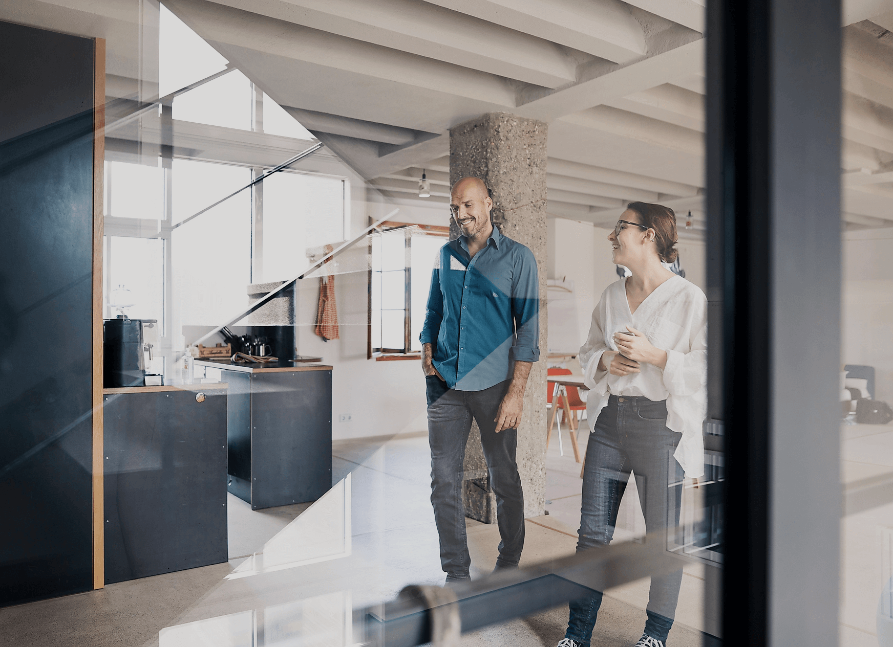 Two people walking and talking in a modern office space with large windows and minimalist furniture.